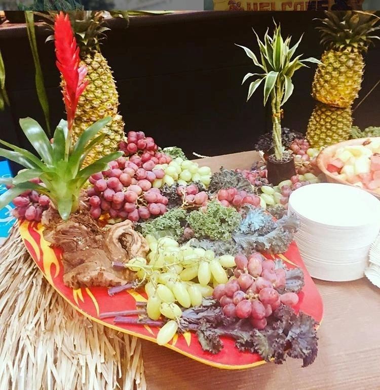 Elaborate Hawaiian luau catering display with fresh tropical fruits, pineapples, grapes, and traditional Hawaiian food arrangement